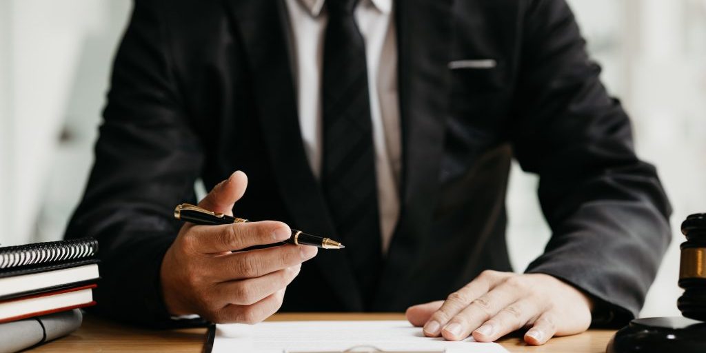 A lawyer sits in his office, on a table with a small hammer to beat the judges desk in court. and justice scales, lawyers are drafting a contract for the client to use with the defendant to sign.