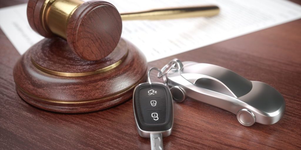 Auction hammer with golden details, a car key next to it and a contract in the background.
